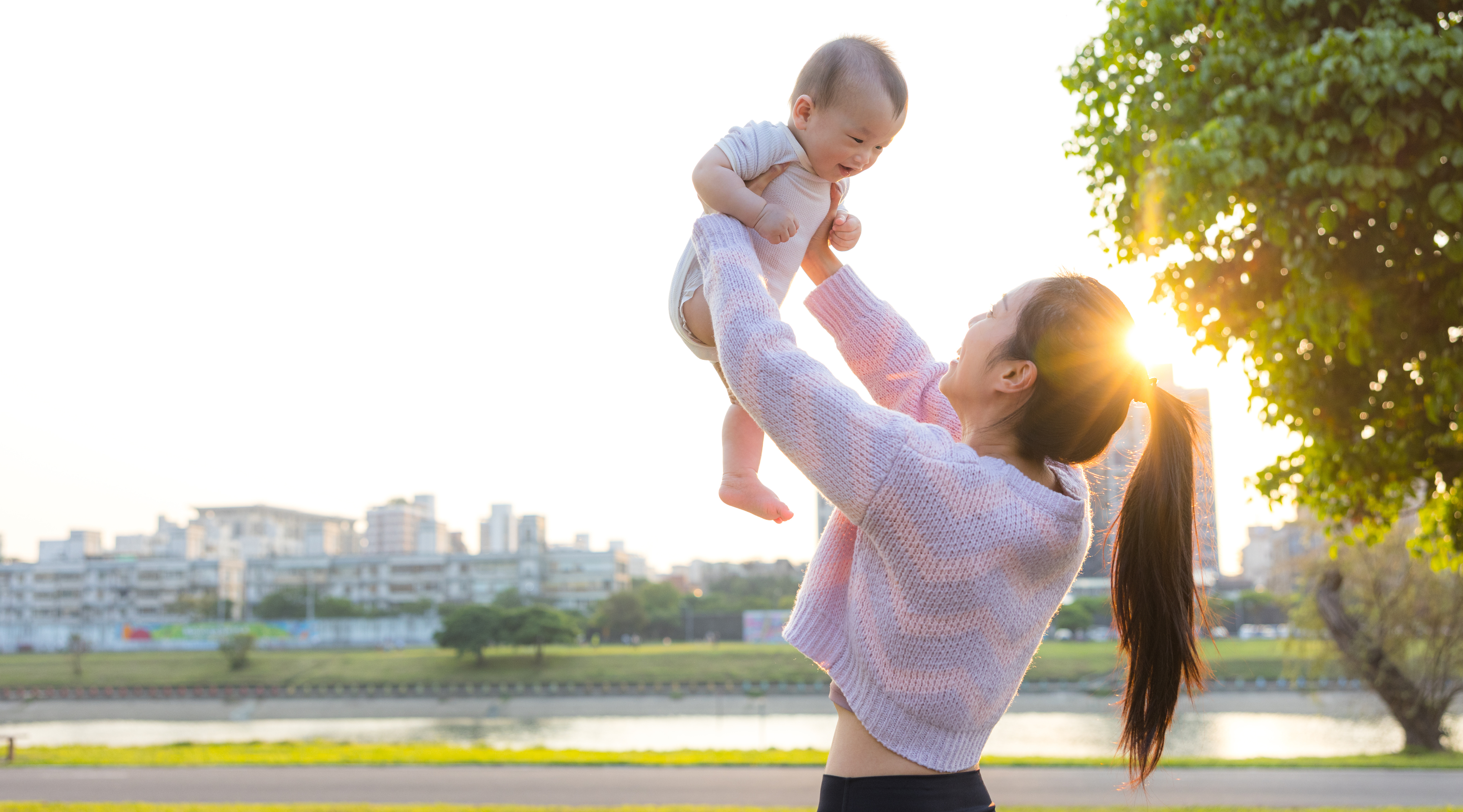 Woman holding a baby outdoors with a cityscape in the background