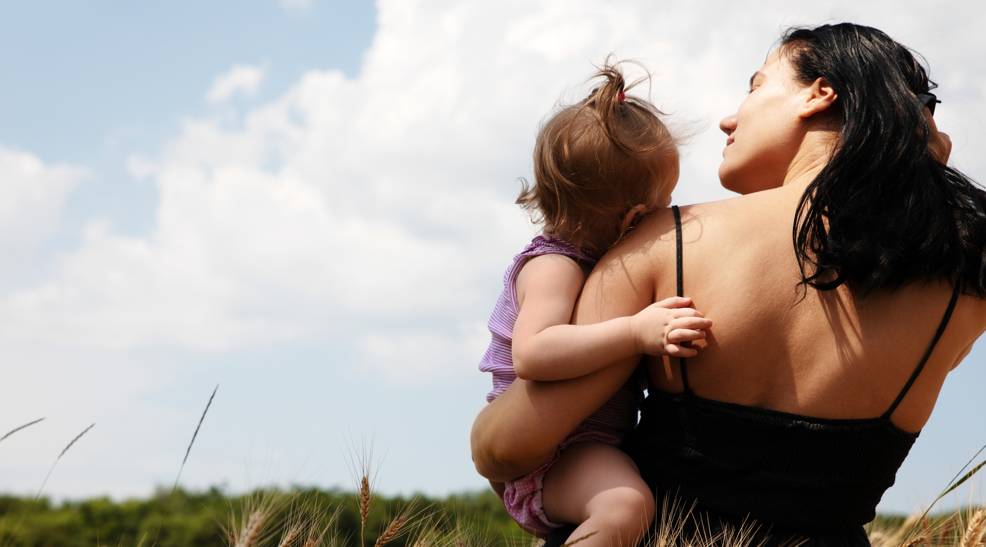 Woman holding a child in a field with a clear sky