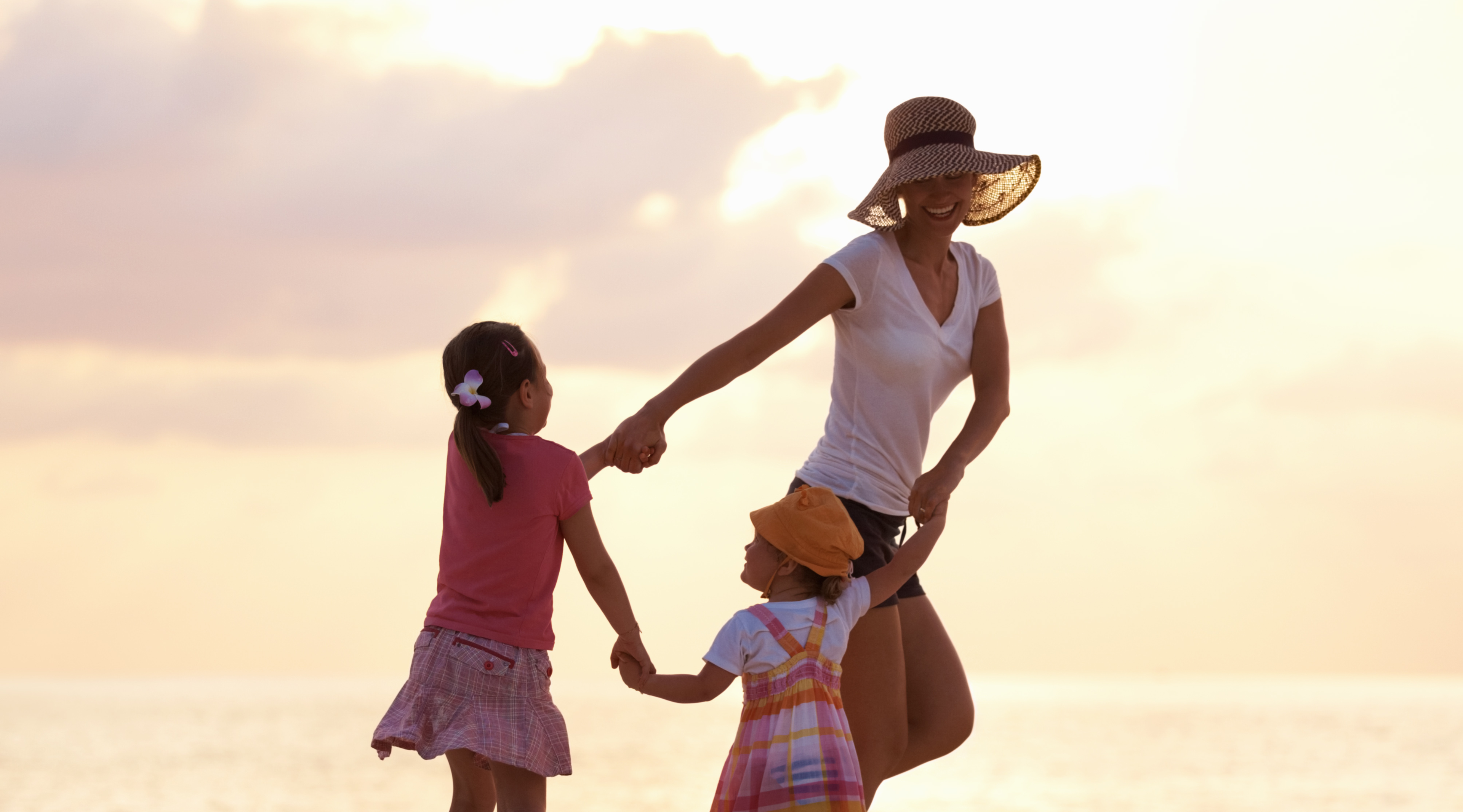 Woman and two children holding hands on a beach at sunset