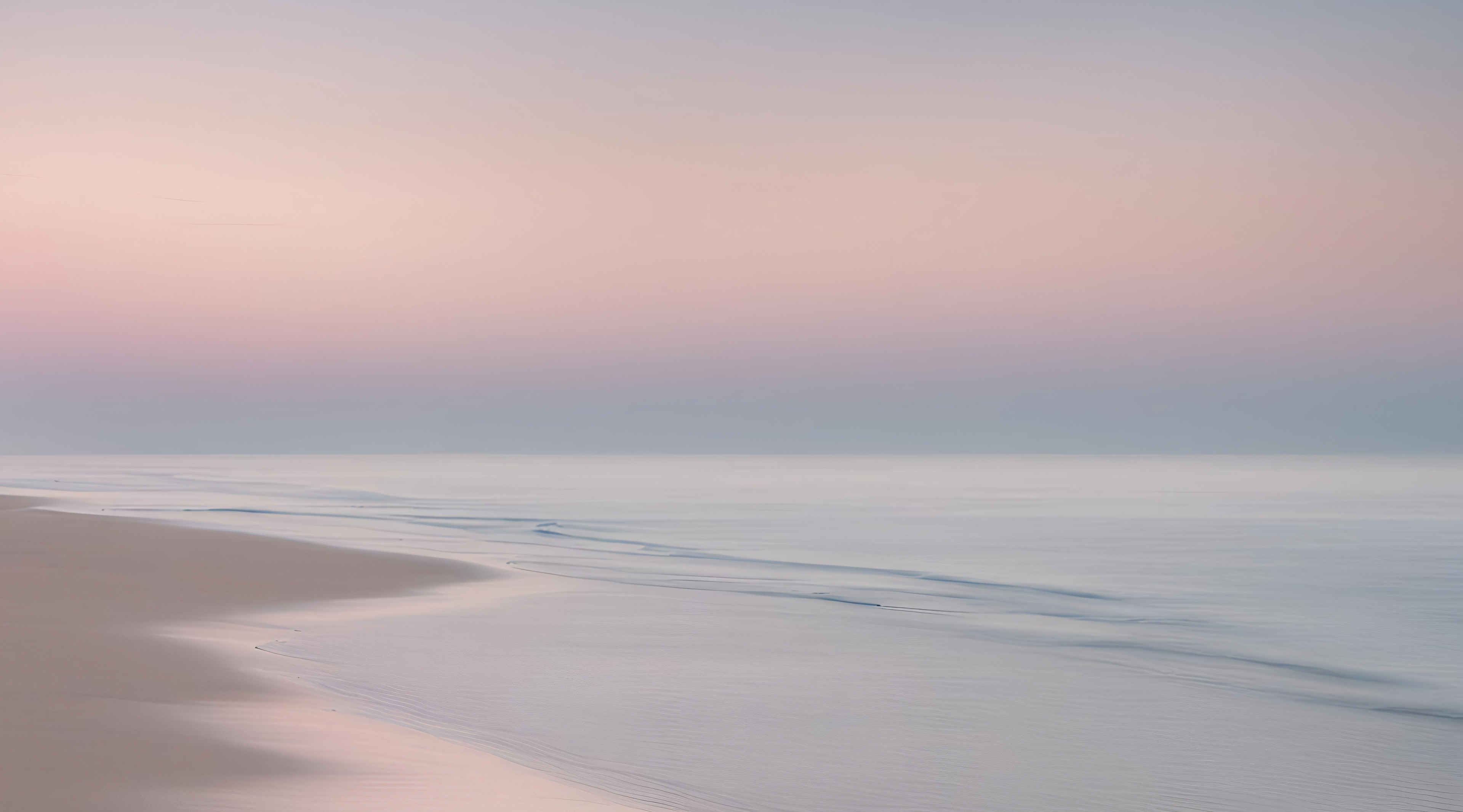 Peaceful beach scene with soft pink and blue colors in the sky.